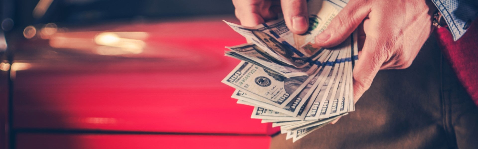 Hands holding a stack of cash in front of a red vehicle