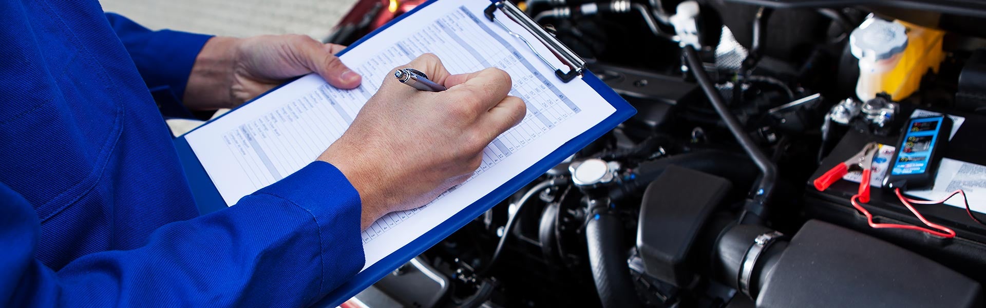 Mechanic filling out a checklist on a clipboard while inspecting an open car engine
